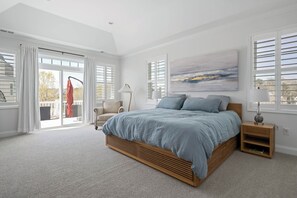 Une chambre à coucher avec un grand lit, une porte-fenêtre coulissante, une chaise et un tableau au mur.