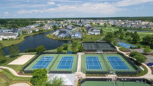 Vista aerea di una zona residenziale con diversi campi da tennis, un lago e case.