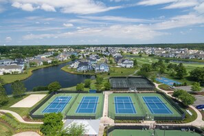 An aerial view of a residential area with multiple tennis courts, a lake, and houses. - 26960 Sunburst Path, The Peninsula (Millsboro)
