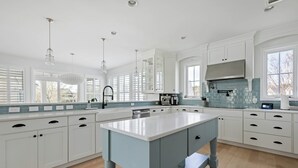 Un'ampia cucina con mobili bianchi, un'isola centrale e un'ampia finestra che garantisce luce naturale.
