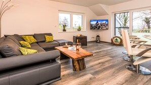 Un salon moderne avec un canapé d’angle, une table basse en bois, un téléviseur et un coin repas avec des chaises.