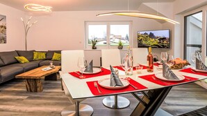 Un salon moderne comprenant un coin repas, un canapé, une table basse et un téléviseur fixé au mur.