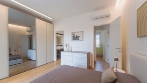 Ein modernes Schlafzimmer mit einem großen Bett, einer Kommode, einem Spiegel und einem durch eine offene Tür einsehbaren Badezimmer.