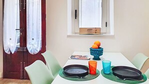A dining area with a table set for two, a window with curtains, and a small window with a wooden box on the sill.