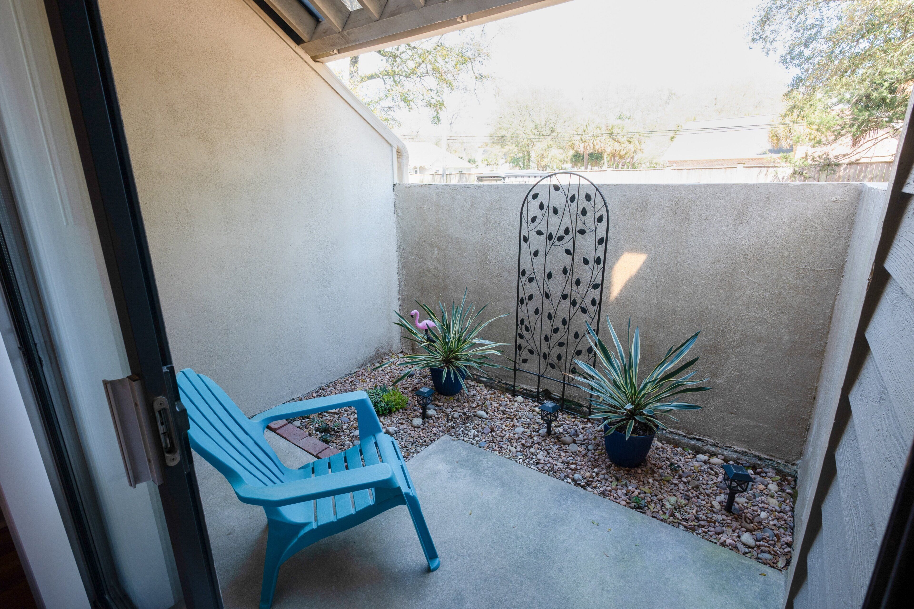 A small outdoor patio with a blue chair, potted plants, and a decorative metal fence.
