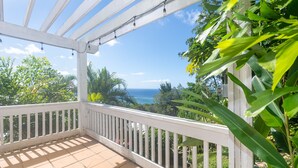A covered balcony with a view of the ocean, surrounded by greenery. - Top Ridge Views 2 Bedroom Home (Roatan)