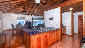 A kitchen with wooden cabinets, a tiled backsplash, and a large island with a sink. - Top Ridge Views 2 Bedroom Home (Roatan)