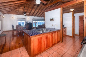 A kitchen with wooden cabinets, a tiled backsplash, and a large island with a sink. - Top Ridge Views 2 Bedroom Home (Roatan)