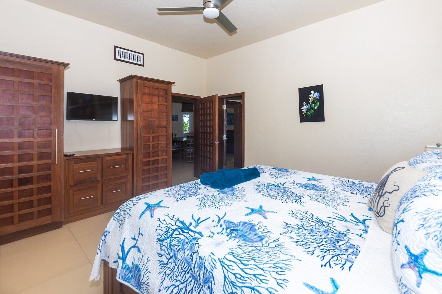 A bedroom with a bed, a TV, wooden cabinets, and a ceiling fan.