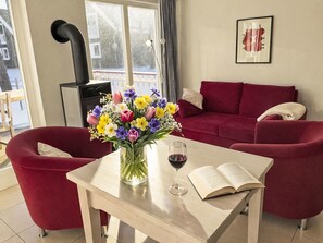 A living room with a red sofa, a table with a book and a glass of red wine, a vase with flowers, and a fireplace. - Strandhaus Glowe by Interhome (Glowe)