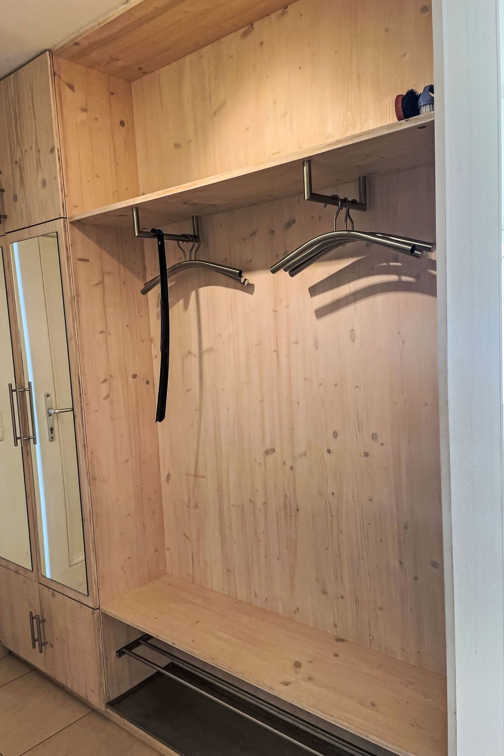Une armoire en bois dotée d’une porte miroir, d’une tringle et d’une étagère.