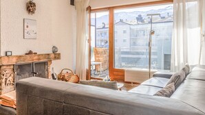 Una sala de estar con sofá, chimenea y vista a edificios y montañas a través de un ventanal grande.