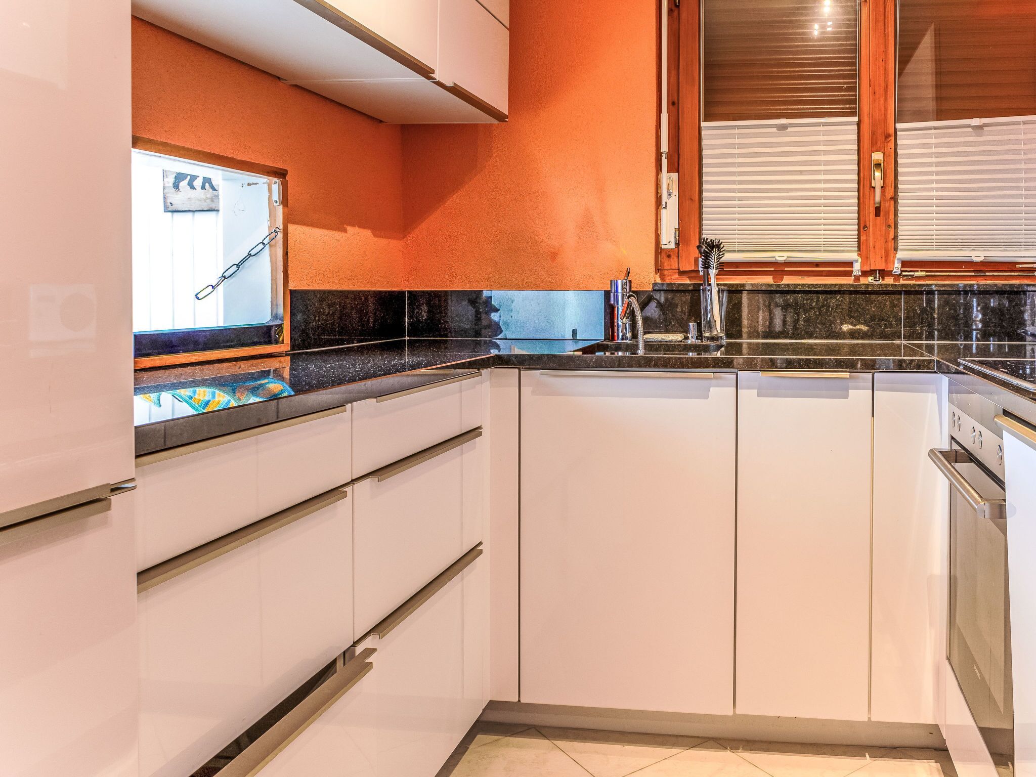 A kitchen with white cabinets, a black countertop, and a window with blinds.