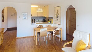 A modern living room with a dining area, wooden flooring, and a kitchen in the background. - Toissa A6 by Interhome (Savognin)