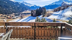 A balcony with a view of snow-covered mountains and a forested valley. - Toissa A6 by Interhome (Savognin)