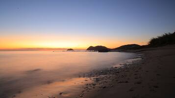 A beach with calm water, a clear sky, and distant landforms.