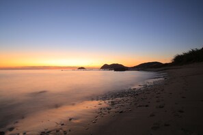 Una playa con aguas tranquilas, cielo despejado y formas de tierra a lo lejos.