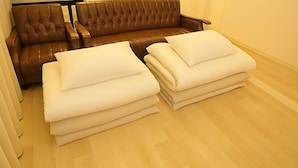 Una habitación con un sofá de cuero marrón y dos montones de almohadas blancas sobre un suelo de madera.