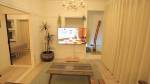 Una sala de estar con televisor, una mesa de madera, una planta en maceta y una araña.