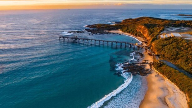 A coastal landscape with a pier extending into the sea, a sandy beach, and a forested area. - Beachside Bliss 3BDR mins to Caves Beach & Bistros (Caves Beach)