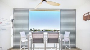 A balcony with a table and chairs, a ceiling fan, and a view of a distant landscape. - Beachside Bliss 3BDR mins to Caves Beach & Bistros (Caves Beach)