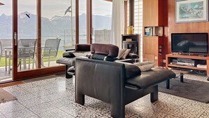 Ein modernes Wohnzimmer mit einem großen Schiebeglasfenster, das auf einen Balkon mit Bergblick führt.