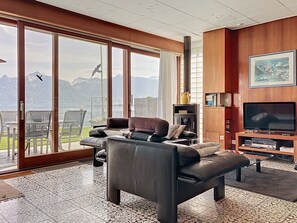A modern living room with a large sliding glass door leading to a balcony with a mountain view. - Villa Bikini by Interhome (St-Gingolph)