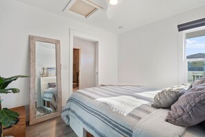 A bedroom with a bed, a large mirror, a plant, and a view of the outside. - Luxury Oceanfront 2 bed | Hot Tub + Private Deck (Saint Augustine)