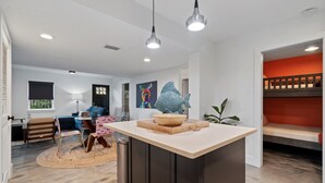A modern kitchen with a central island, pendant lighting, and a dining area with a round table and chairs. - Oceanfront Ground Level Apt | Patio + Beach Access (St. Augustine)