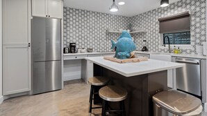 A modern kitchen with a central island, bar stools, a stainless steel refrigerator, and patterned wallpaper. - Oceanfront Ground Level Apt | Patio + Beach Access (St. Augustine)