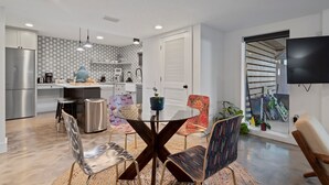 A modern kitchen with a dining area, a TV mounted on the wall, and a staircase leading to another level. - Oceanfront Ground Level Apt | Patio + Beach Access (St. Augustine)