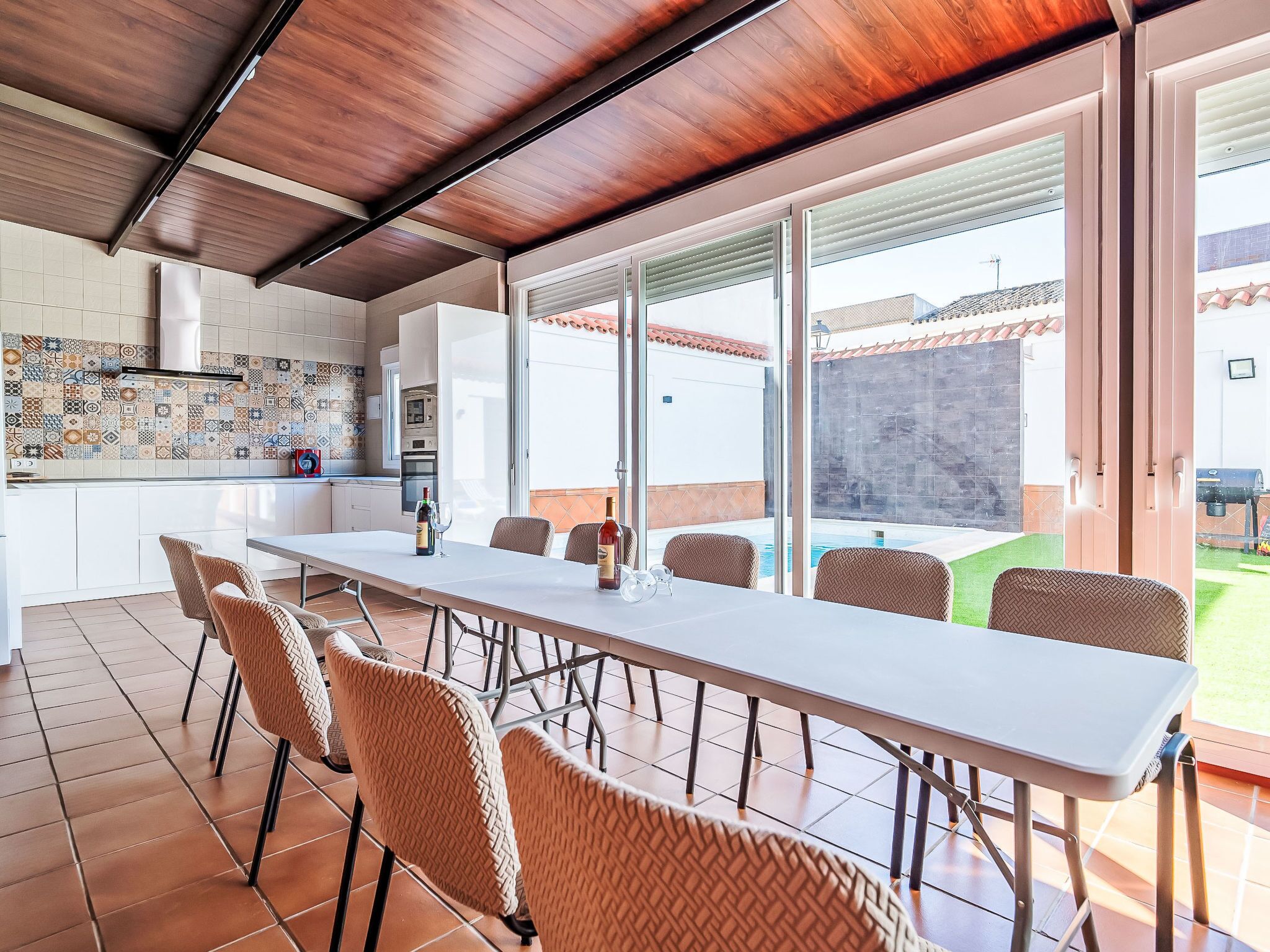 A modern kitchen with a tiled backsplash, a dining area with a table and chairs, and a view of a swimming pool.
