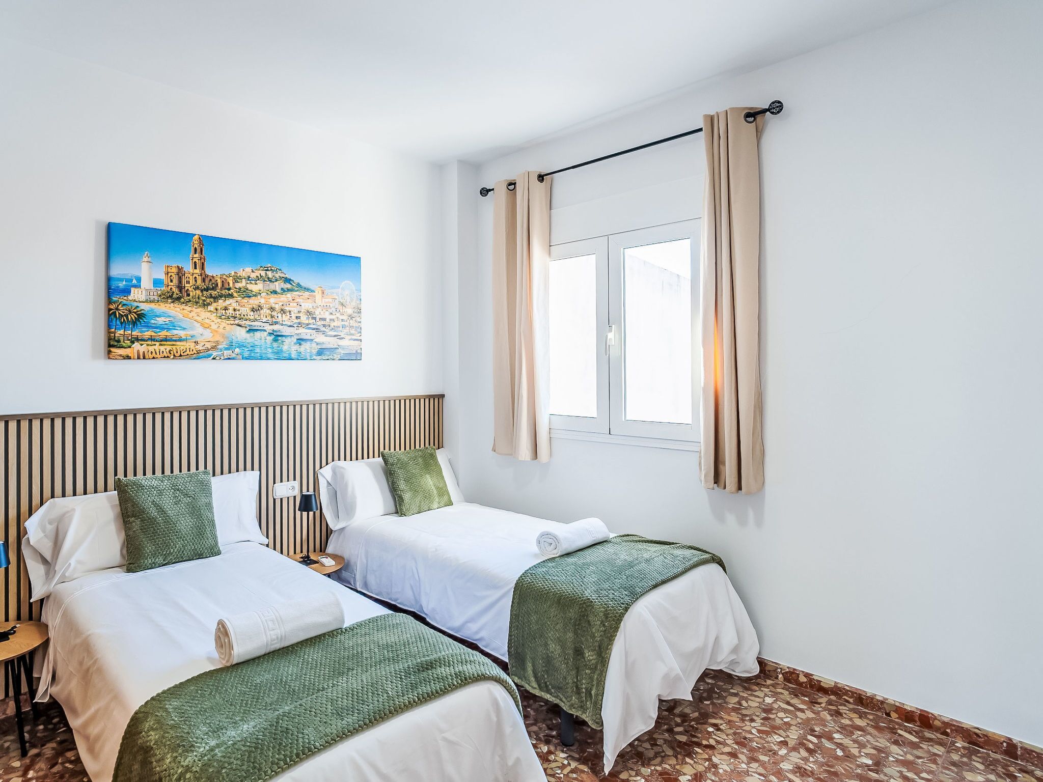 A hotel room with two beds, a window with curtains, a painting of a coastal scene, and a tiled floor.