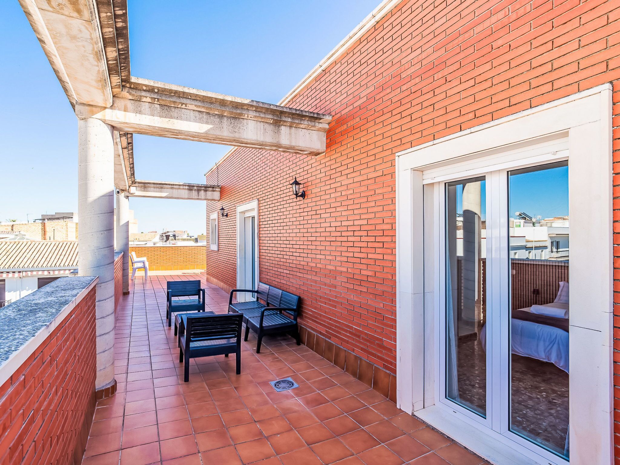 Eine Dachterrasse mit Backsteinmauer, Schiebeglastür und zwei schwarzen Stühlen.