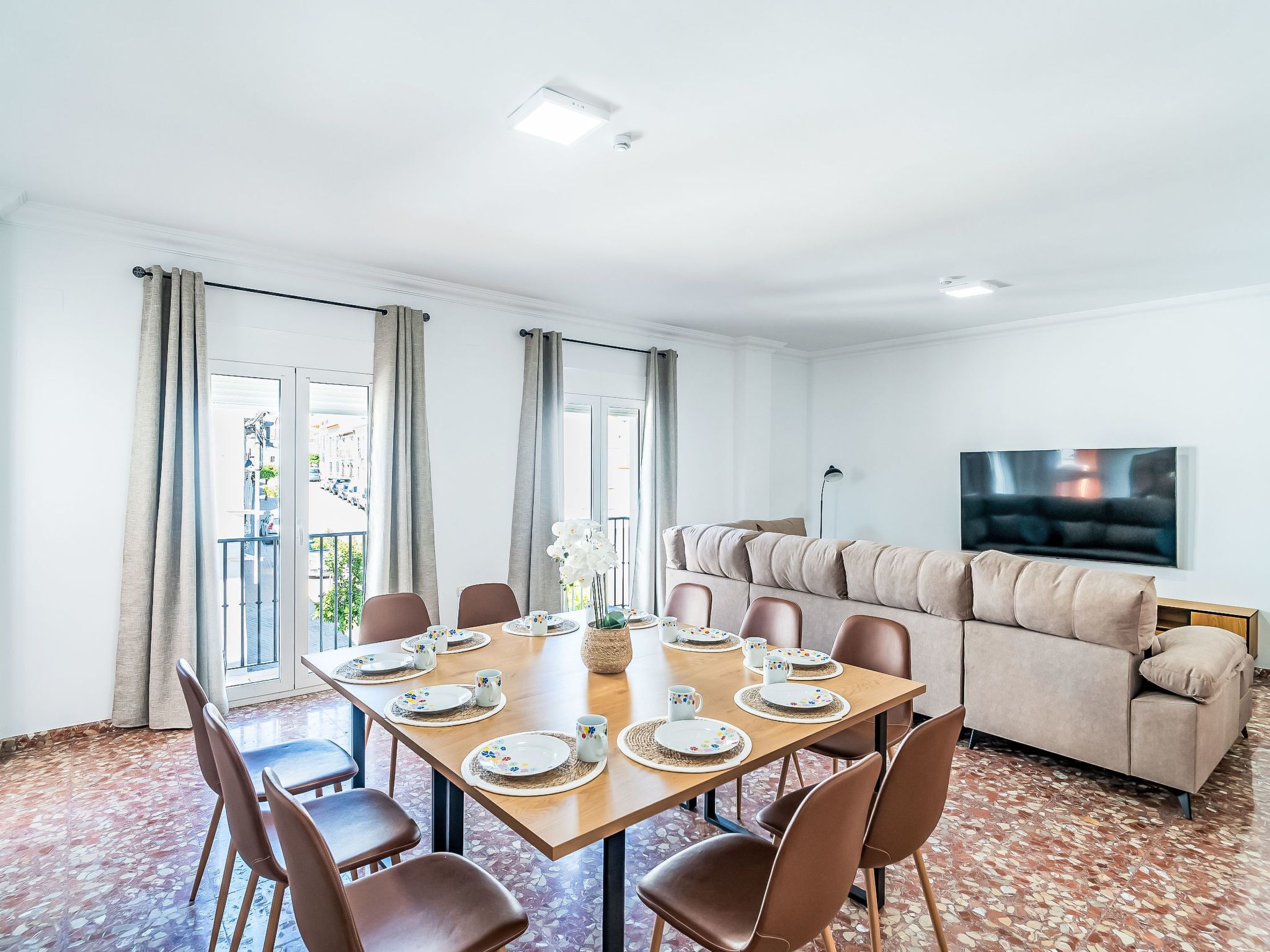 Un coin repas avec une table dressée pour quatre personnes, un canapé et un téléviseur fixé au mur.
