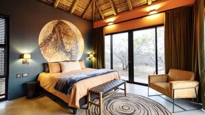 Ein Schlafzimmer mit Bett, einer Bank, einem Sessel und einem großen, runden Kunstwerk, mit Blick durch ein Fenster.