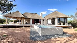Eine moderne Villa mit Swimmingpool, Sitzgelegenheiten im Freien und strohgedeckten Gebäuden.