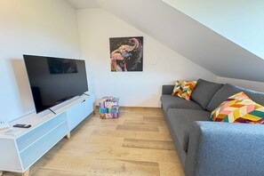 A modern living room with a flat-screen TV, a grey sofa, colorful cushions, and a wooden floor. - Southwest Ljubljana Private Parking 3 (Ljubljana)