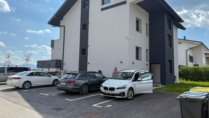 A modern building with a parking lot, several cars, and a trash bin. - Southwest Ljubljana Private Parking 3 (Ljubljana)