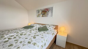 A neatly made bed with a floral bedspread, a bedside table with a lamp, and a painting on the wall. - Southwest Ljubljana Private Parking 3 (Ljubljana)