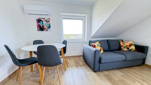 A room with a gray sofa, a round table with chairs, a window, and a colorful painting on the wall. - Southwest Ljubljana Private Parking 8 (Ljubljana)