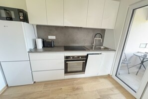 Eine moderne Küche mit weißen Schränken, einer Edelstahl-Spüle, einem Backofen und einer Mikrowelle.