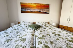 Ein Schlafzimmer mit einem Bett, einem Wandbild von einem Sonnenuntergang, Nachttischlampen und einem Kleiderschrank.