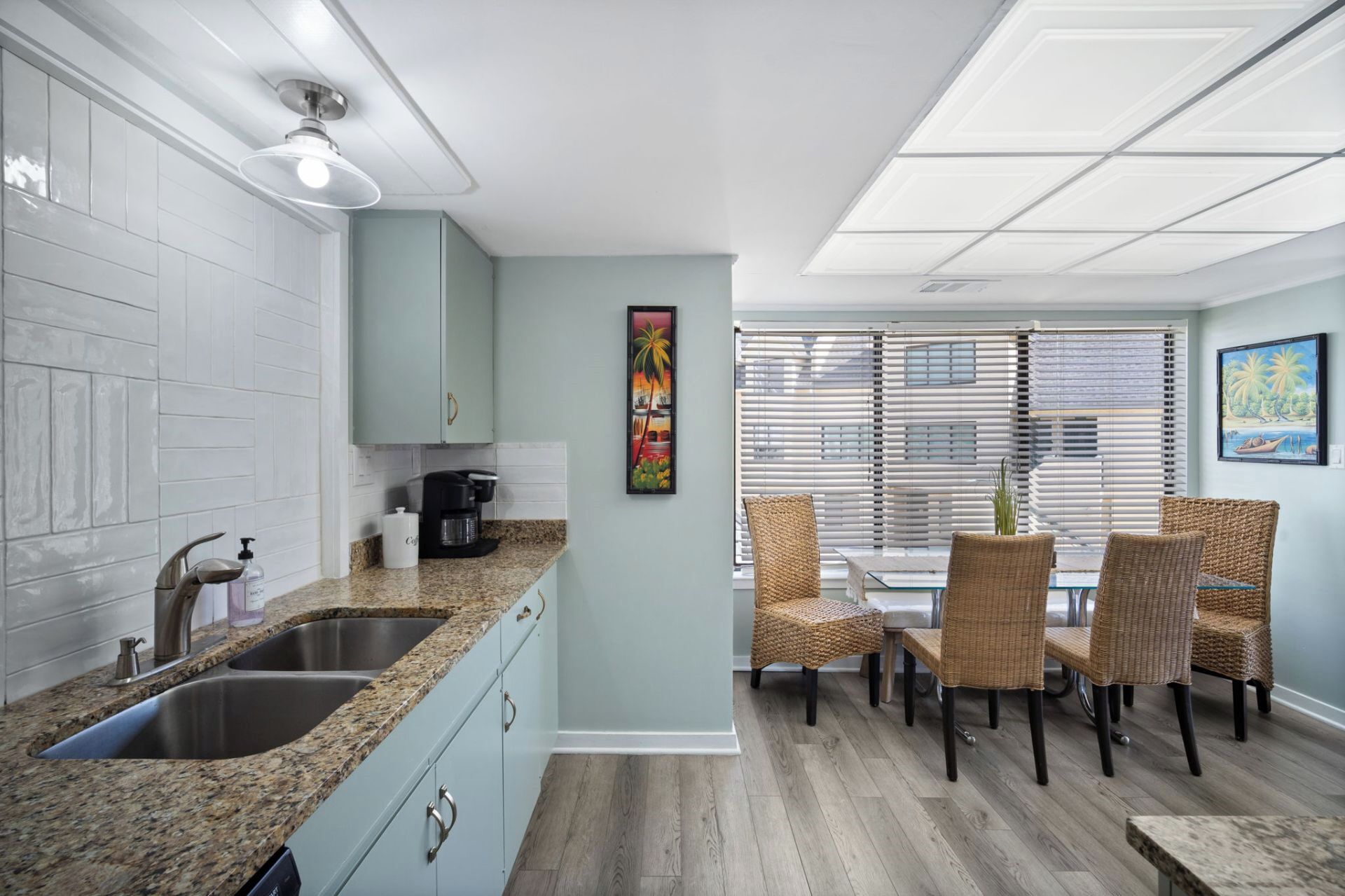 A modern kitchen with granite countertops, stainless steel appliances, and a dining area with wicker chairs and a glass table.