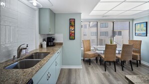 A modern kitchen with granite countertops, stainless steel appliances, and a dining area with wicker chairs and a glass table. - New to VRBO 3 Bedroom Villa - Golf cart included - 604 Newhaven (Fripp Island)