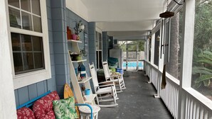 A covered porch with a red floral sofa, white rocking chairs, and a small table. - Huge Private Pool, Single Level Easy Access, 2 Golf Carts Included, Pet Friendly - 276 Tarpon Blvd (Fripp Island)