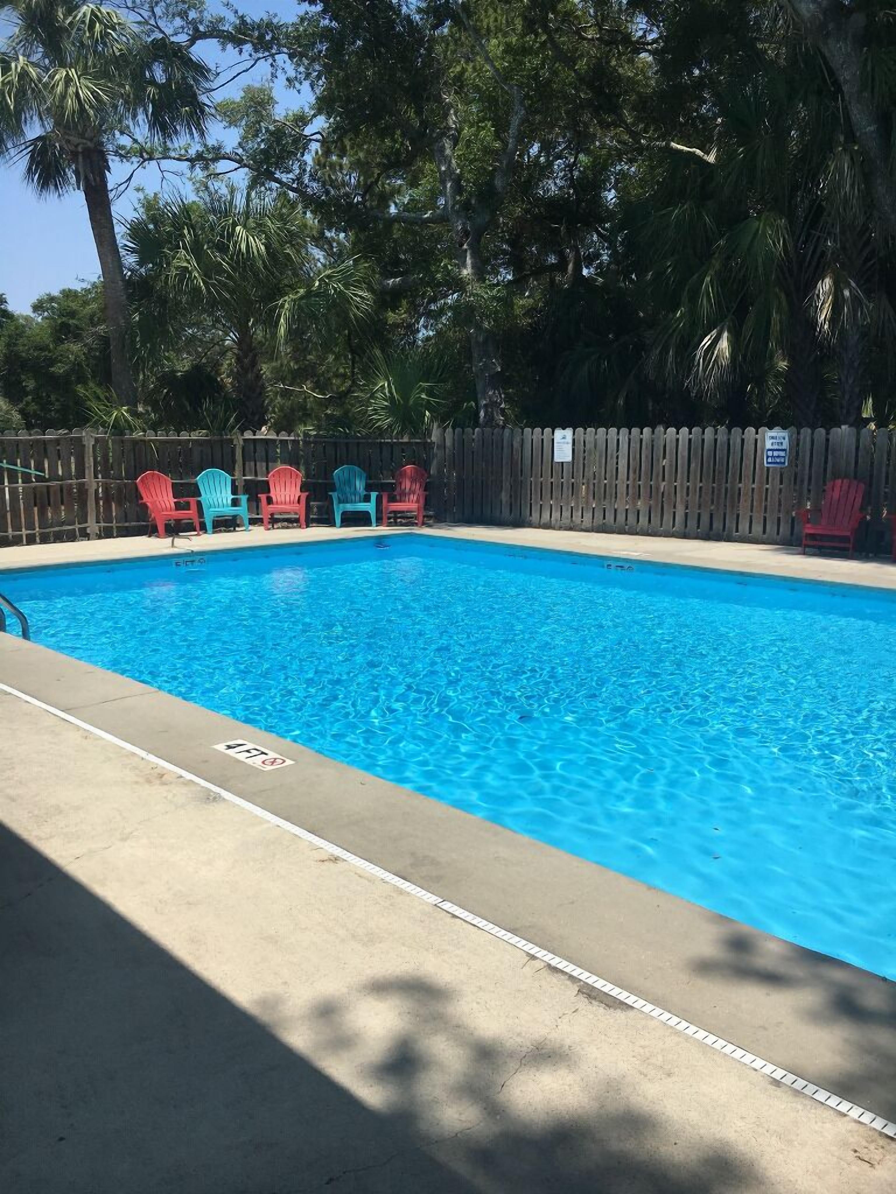 Piscina retangular com superfície de água azul, rodeada por uma cerca de madeira.