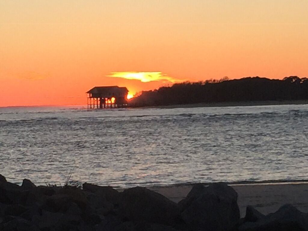 A sunset over a body of water with a structure on stilts in the distance.