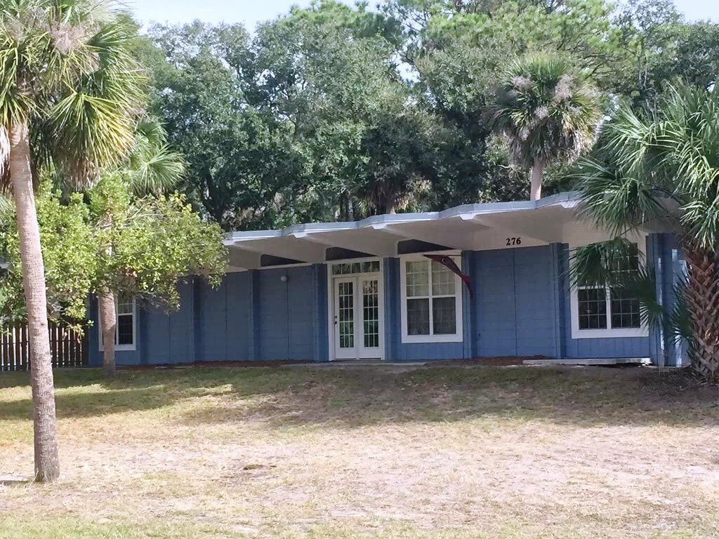 A single-story house with a covered porch, numbered 276, surrounded by trees and a grassy yard.