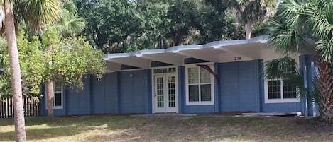 A single-story house with a covered porch, numbered 276, surrounded by trees and a grassy yard.